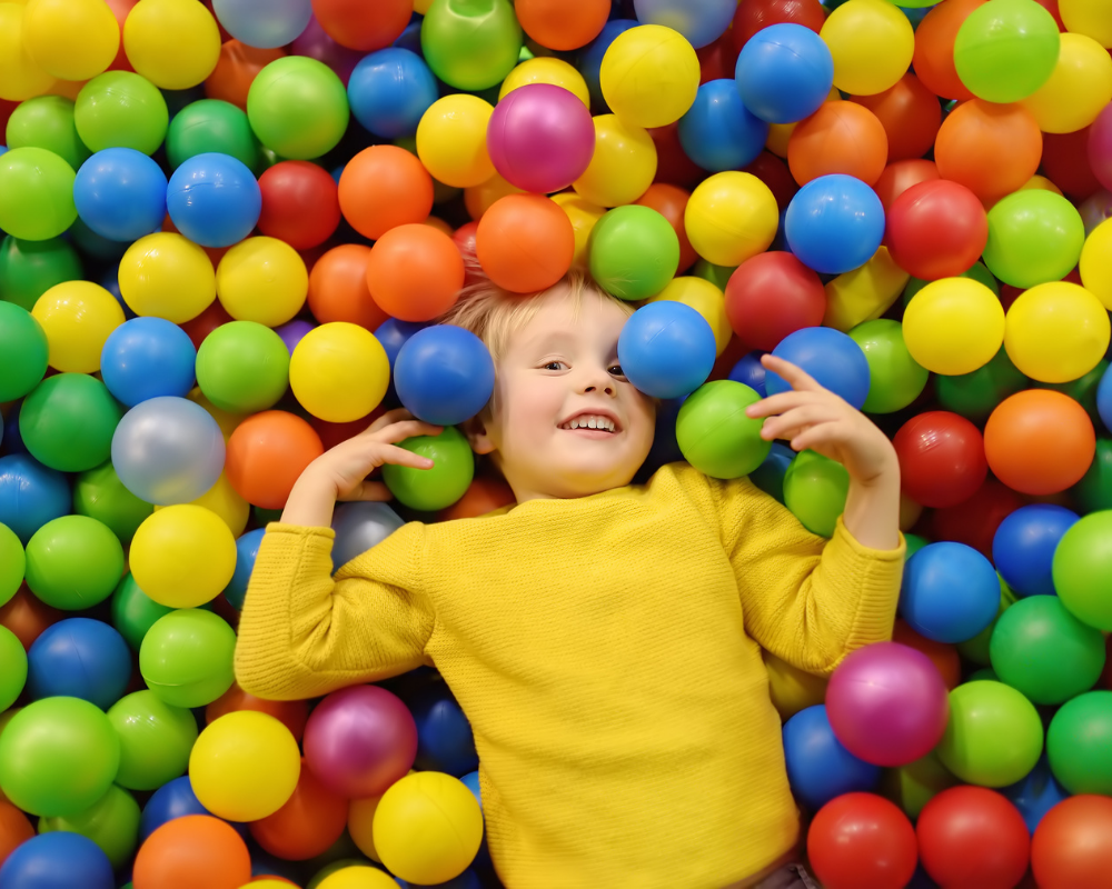 Barn med gul tröja i bollhav med bollar i många olika färger.
