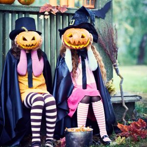 Barn utklädda till häxor håller Halloween-pumpa framför sina ansikten