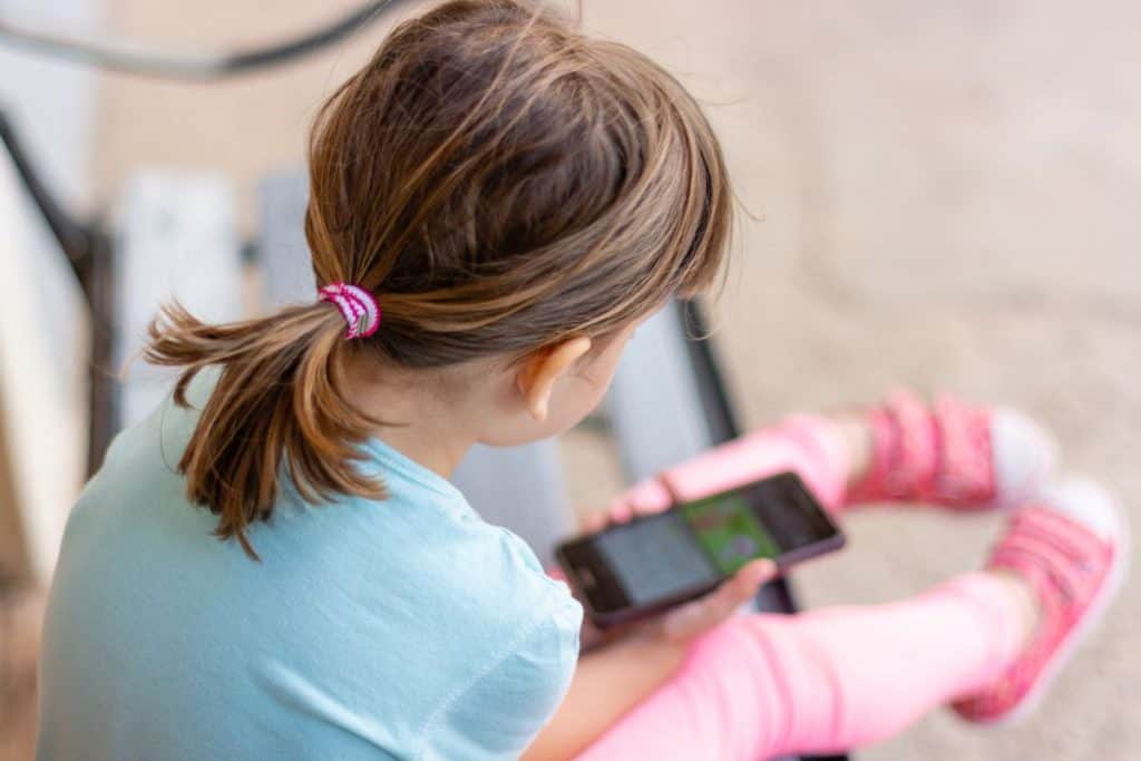 Flicka fotat bakifrån, leker med sin mobiltelefon